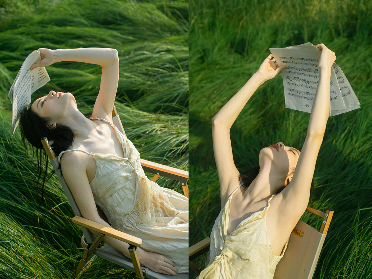 一位穿着连衣裙的年轻女子坐在绿草地上的一把椅子上 举着一本书在头顶上 旁边有一幅女人躺在床上的画。