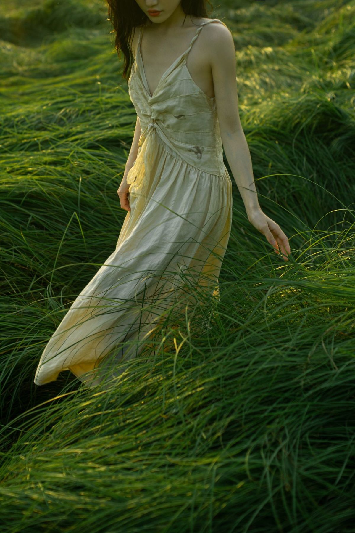 一位穿着白色连衣裙的年轻女子穿过茂密的草丛。