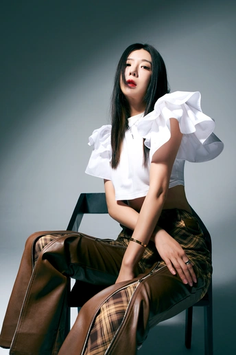 一个穿着白色衬衫和棕色裤子的年轻美女坐在椅子上 双腿交叉。