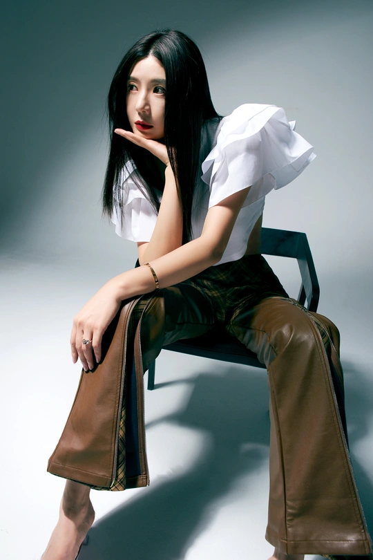 一位穿着白色衬衫和棕色裤子的年轻美女坐在小凳子上 双腿交叉 穿着白色衬衫。