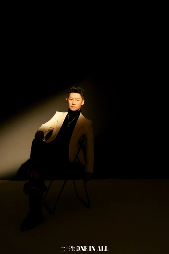 一个穿着西装的男人坐在一个光线昏暗的房间里的一把椅子上。