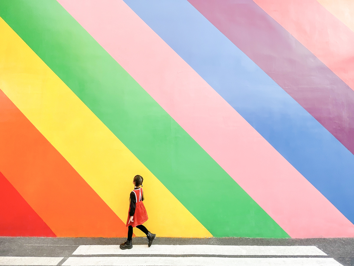 一位穿着红裙子的女孩走过一个彩色墙前面的街道