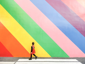 一位穿着红裙子的女孩走过一个彩色墙前面的街道