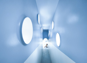 一条长长的走廊 墙壁是白色的 有圆形窗户 一个人在走隧道。