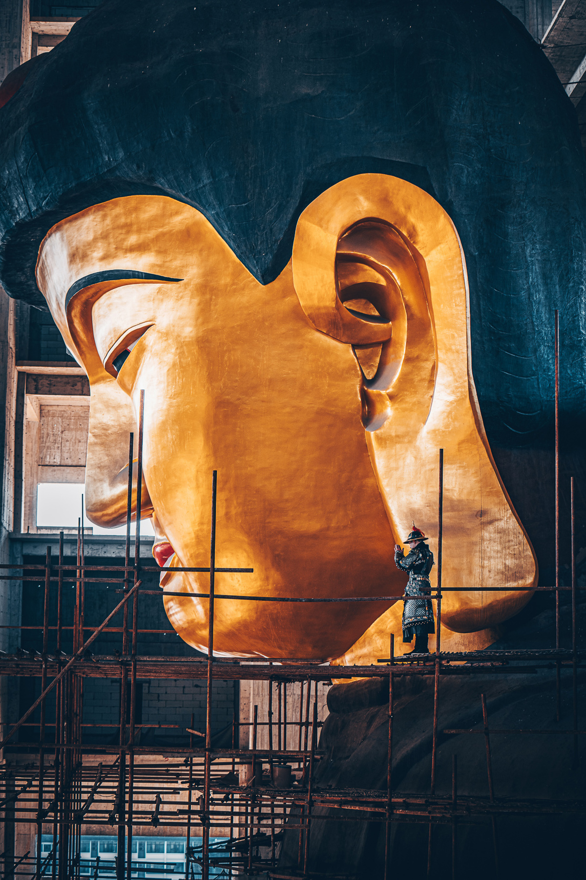 一位视觉艺术家在建筑物内部用脚手架悬挂了一个金色的头像雕塑。