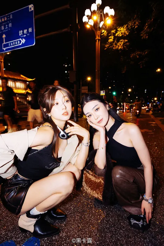 两位年轻女士在夜晚坐在街道的角落里为拍照摆姿势。