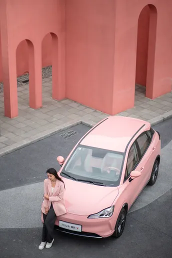 一位女性坐在停在小型粉色汽车旁边