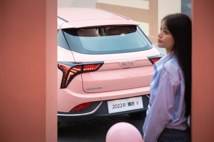 一个站在建筑外 带着粉色汽车和气球的年轻女子