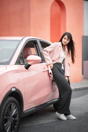 一位穿粉色衬衫的女性靠在粉色汽车旁摆姿势