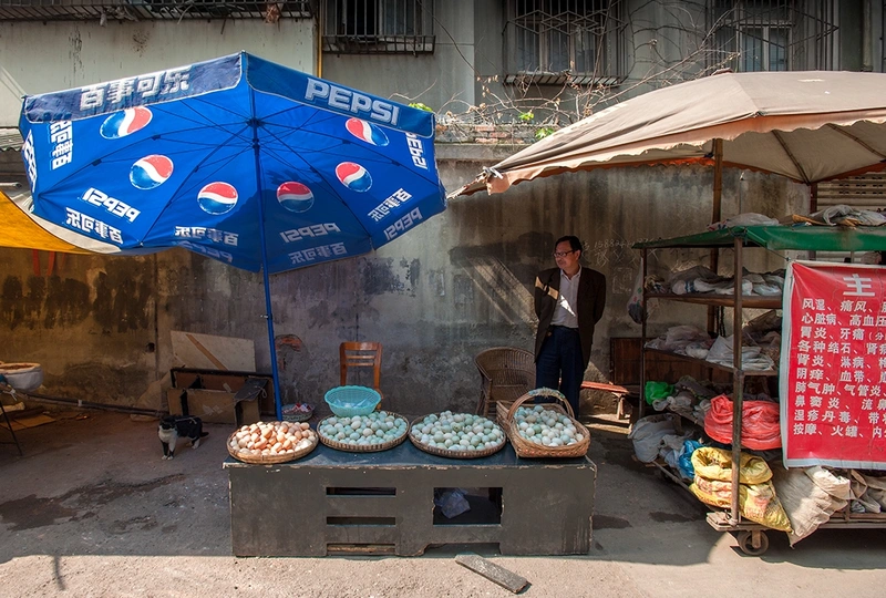 一位站在蓝色雨伞下的女士 旁边是售卖食物的桌子。