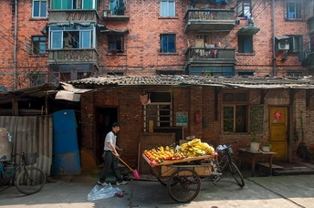 一个推着满载香蕉和其他水果蔬菜的小推车的人走在公寓楼前的一条街上。