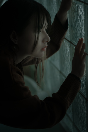 一个年轻女子站在一个黑暗的房间里 透过窗户看外面的光线穿过玻璃。