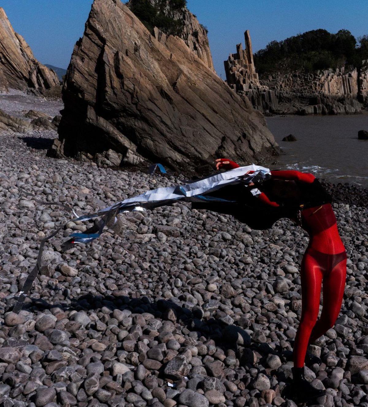 一个 woman 在岩石海滩上放风筝 一个 man 在岸边站着。