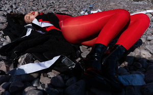 一位穿着红色西装和红色紧身裤的女子躺在岩石海滩上