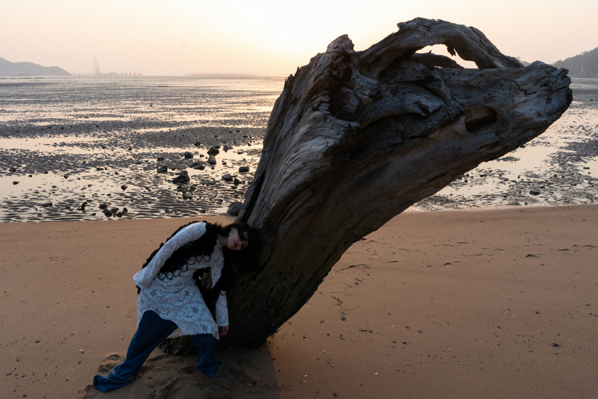 一个人和一个女人在沙滩上亲吻 背景中有大量的漂流木 沙滩后面是水和海浪。