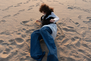 一个年轻女子穿着牛仔裤坐在海滩的沙子上