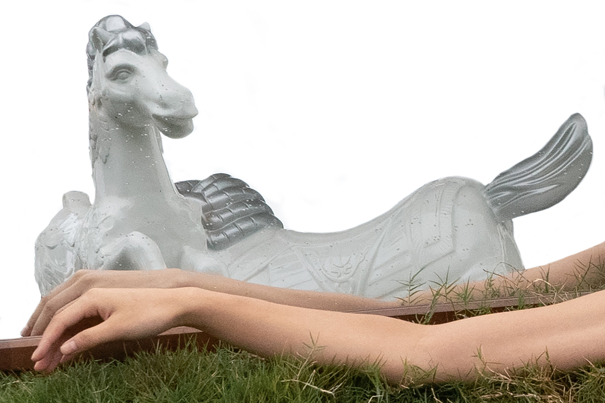 一个年轻女子躺在草地上 手放在一匹马的雕像上。