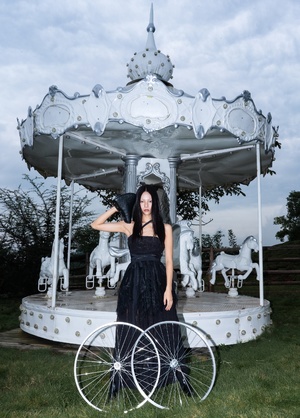 一个穿着黑色连衣裙的年轻女子站在一个旋转木马前面 自行车轮在她身后。