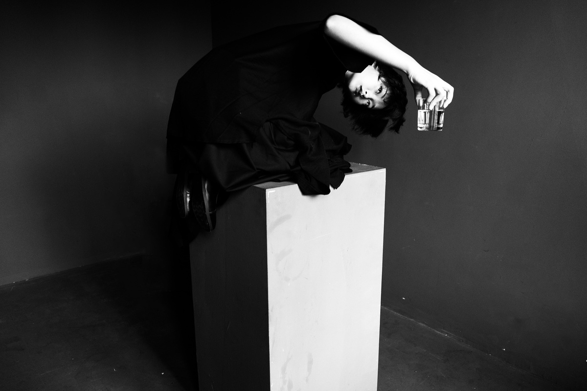 一位穿着黑色连衣裙的女人倚靠在一个白色盒子旁边 盒子顶部放着一瓶瓶装饮料