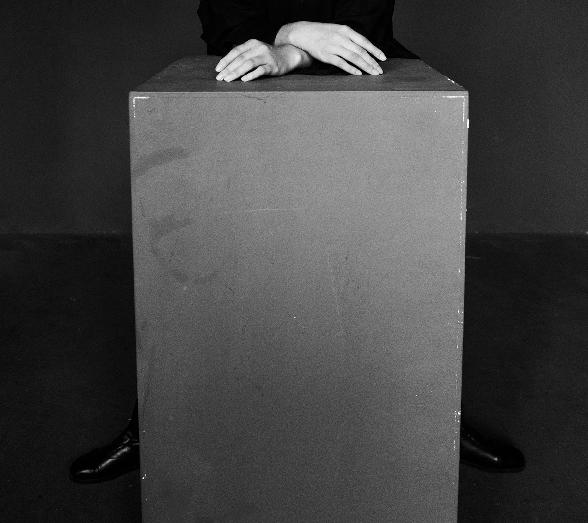 一张黑白照片 一位女子正在桌子旁边 双手放在一个盒子上面。