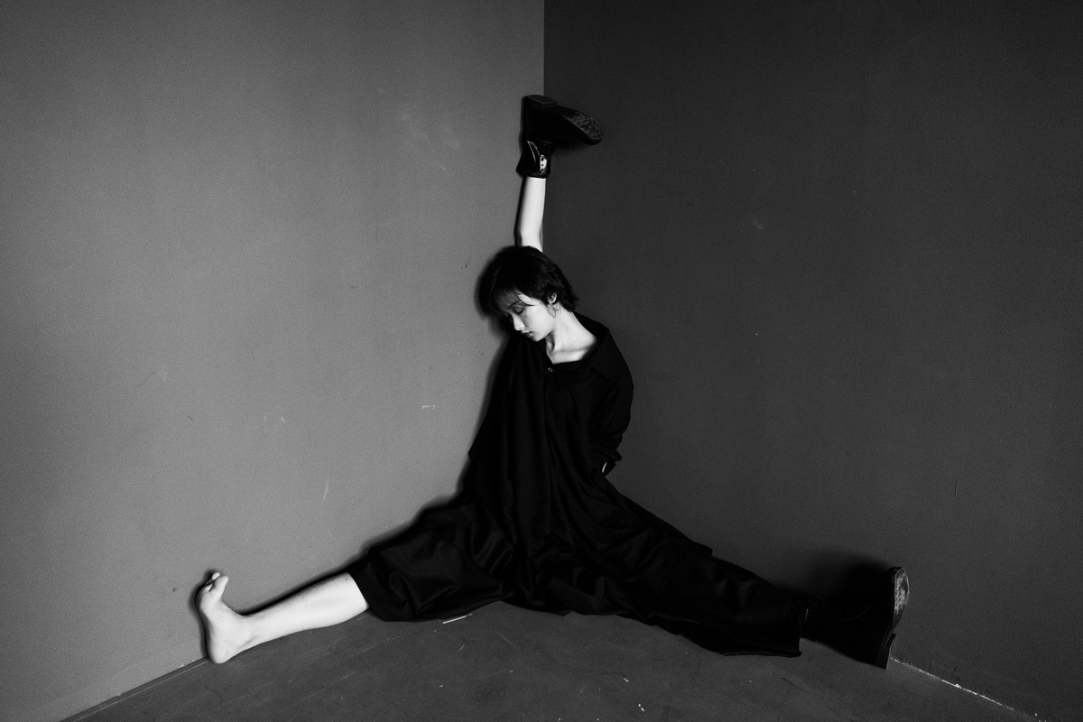 一个穿黑色紧身衣的女人 双腿交叉坐在地板上 面对一面墙。