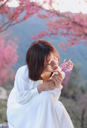 一位年轻女子抱着一朵白色花朵 闻着粉红色樱花的花香。