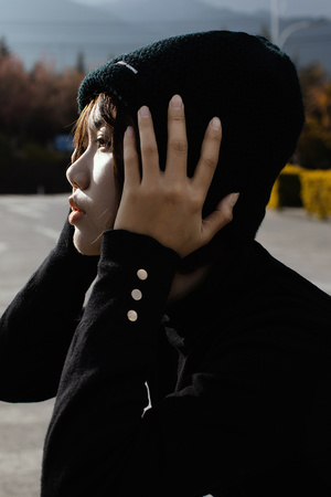 一个穿着黑色外套的年轻人站在停车场 双手捂住脸。