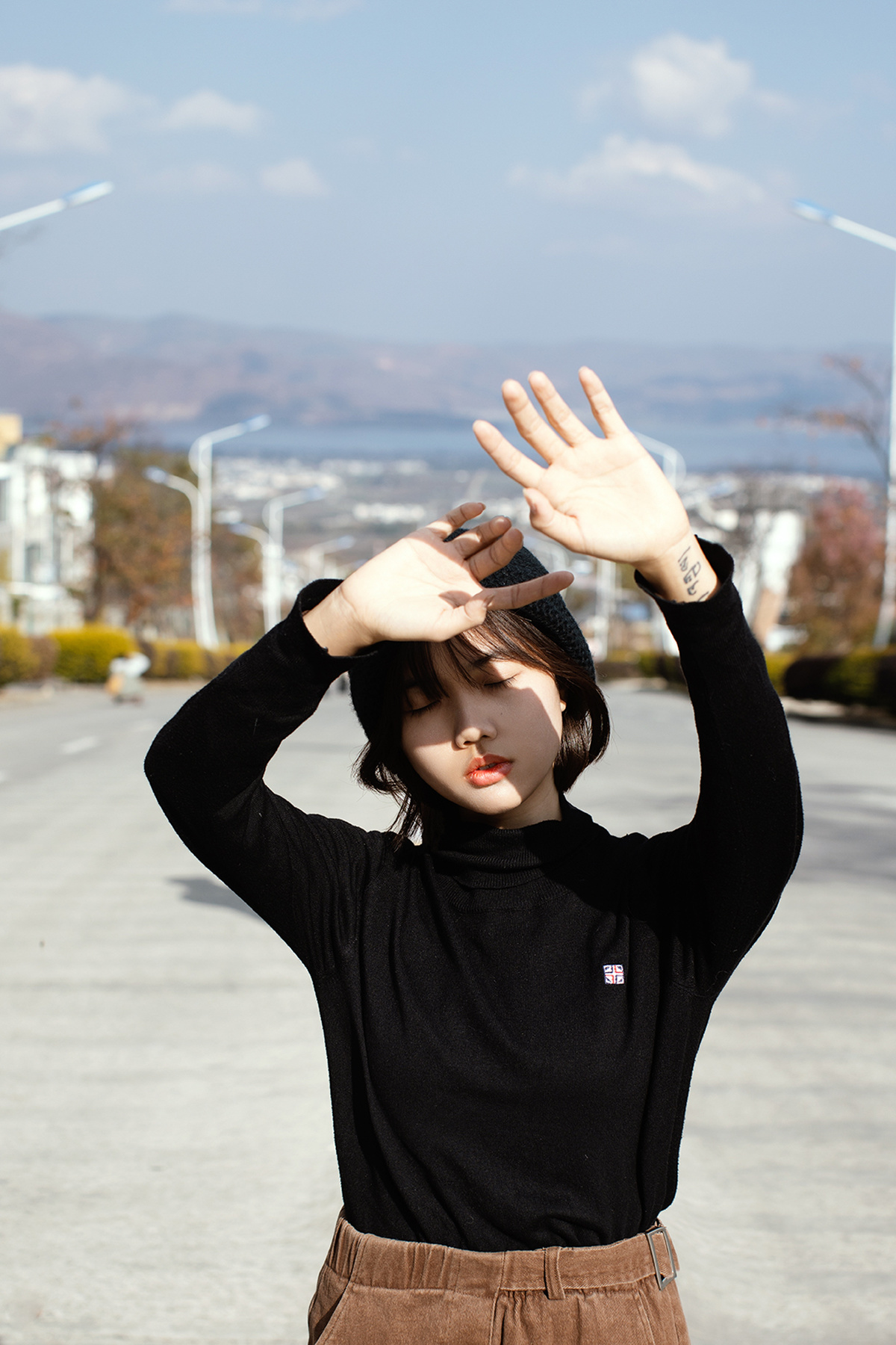 在停车场前 一个穿黑色衣服的年轻女子举起双手挡住眼睛前的交通标志。