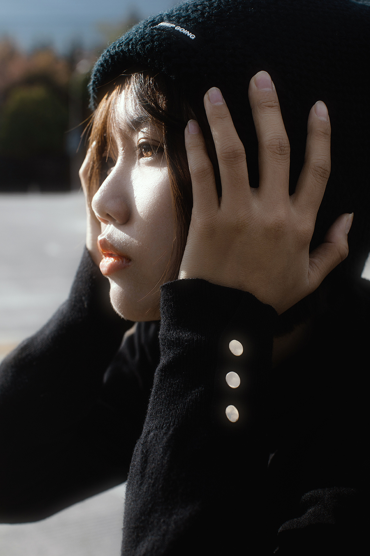 一个戴黑色外套和黑色帽子 用双手遮住脸的年轻女子