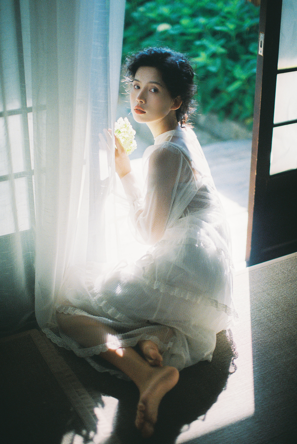 一位穿着白色连衣裙的年轻女子抱着花坐在窗户前