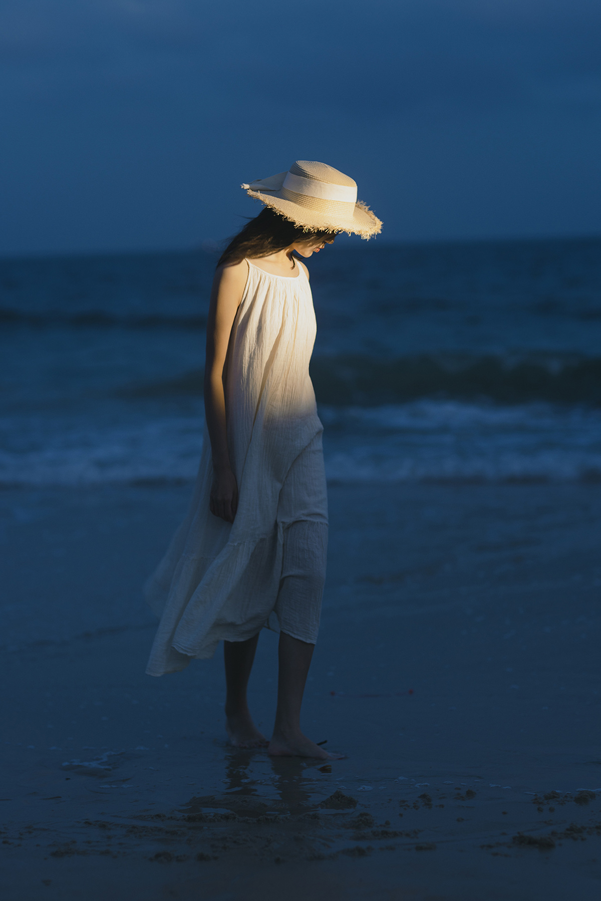 一个穿着白色连衣裙和帽子站在夜晚水中的年轻女子