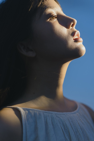 一位年轻女子闭着眼睛仰望着蔚蓝的天空 阳光照耀在她身上。