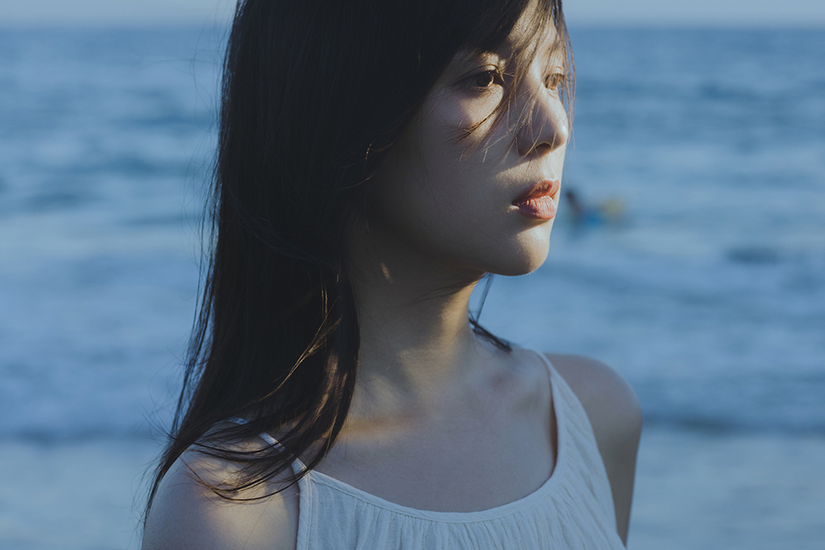 一位穿着白色连衣裙的年轻女子站在海滩上 眺望着大海。