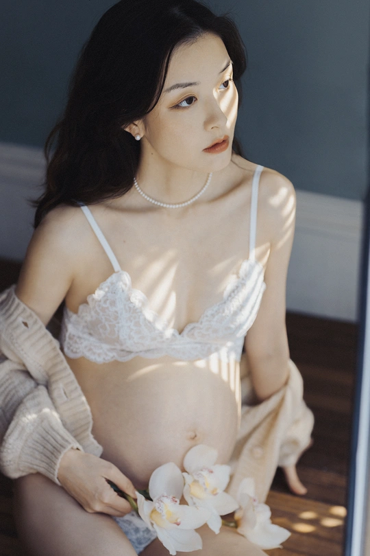 一位年轻女子坐在镜子前地板上 抱着白色花朵放在肚子上。
