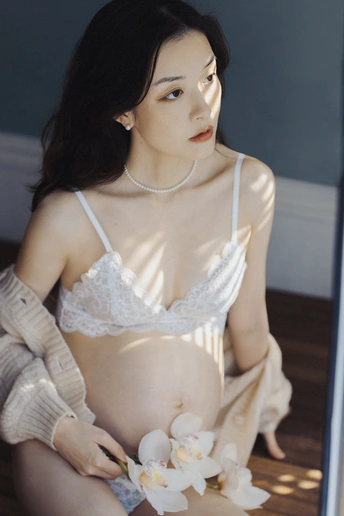 一位年轻女子坐在镜子前地板上 抱着白色花朵放在肚子上。