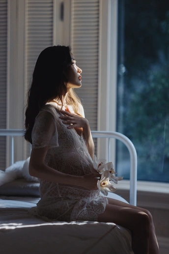一个年轻女子坐在昏暗的床边 手里拿着一只白色的泰迪熊。