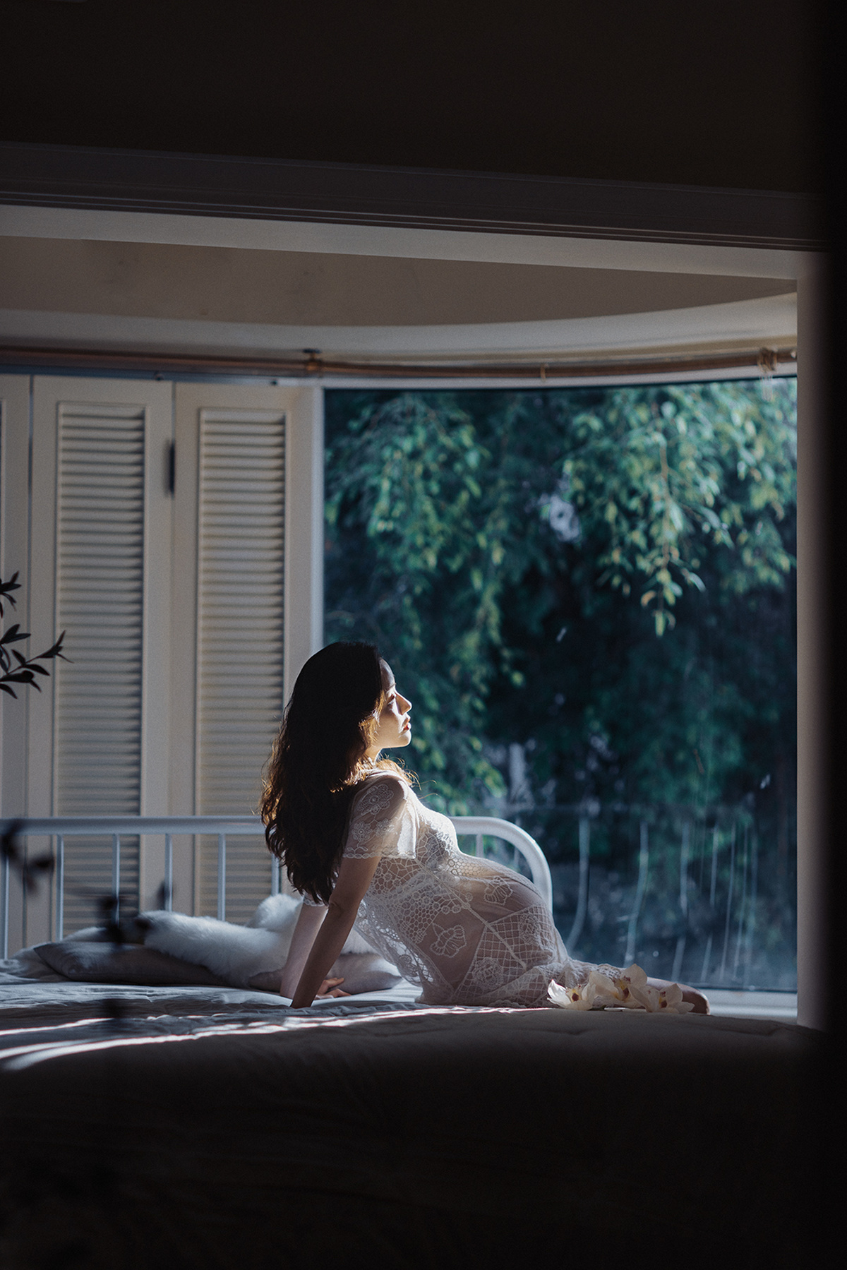 一个穿着白色连衣裙的年轻女子坐在床上 一只猫在房间的窗户附近。