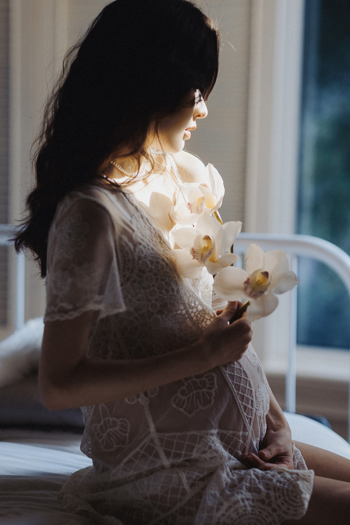 一位怀孕的妇女穿着一件白色连衣裙 手里拿着花 坐在床上。