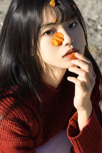 一位穿着红衣服的年轻女子正在吃一个橙子。