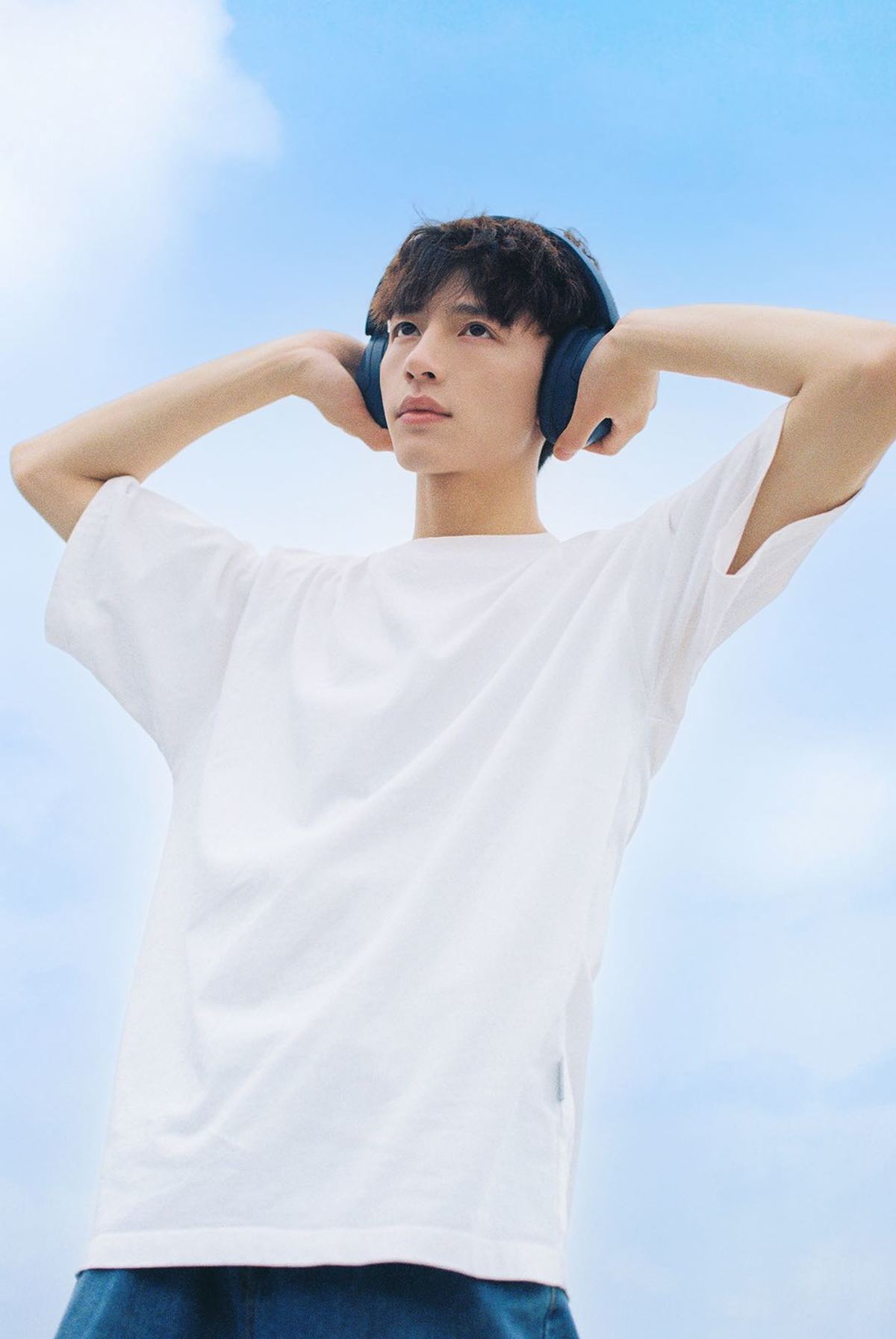 一个戴白色耳机年轻人站在蔚蓝的天空下