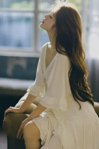 一个穿着白色连衣裙的女人坐在被阳光照亮的椅子上