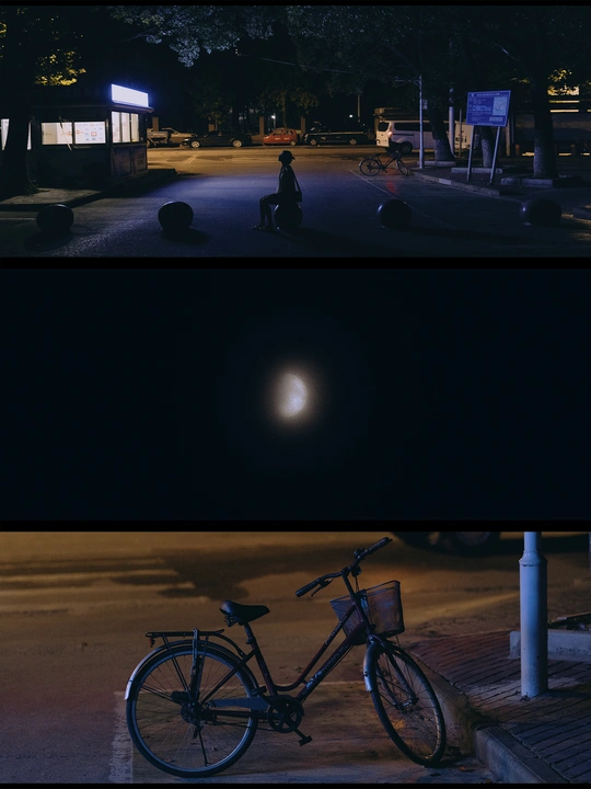 图片显示了一个夜晚的停车场和一条夜晚的街道 有月亮和一个人坐在自行车旁边。