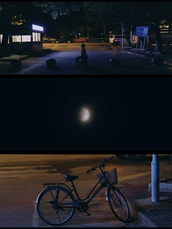 图片显示了一个夜晚的停车场和一条夜晚的街道 有月亮和一个人坐在自行车旁边。