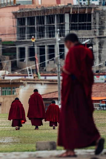 一排穿着红色长袍的人走在一栋正在施工的建筑前的草地上