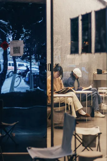 一个在咖啡馆里阅读书籍的男人 而一个女人坐在桌子旁的一把椅子上。