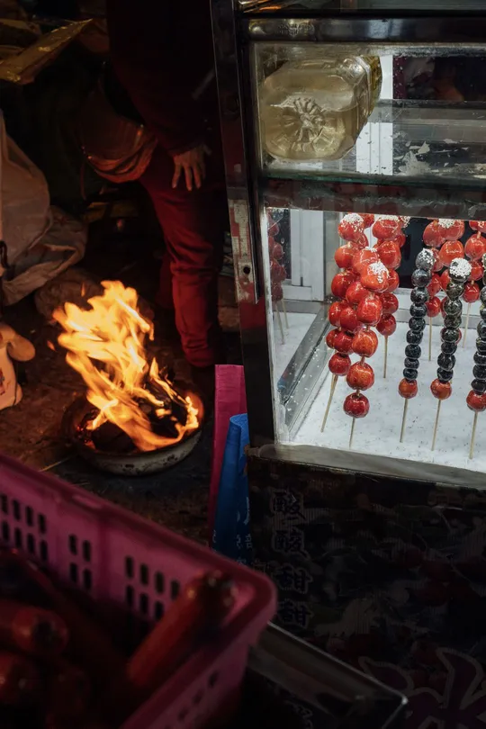 一个男人在展示柜上用火焰烤着木棍上的番茄。