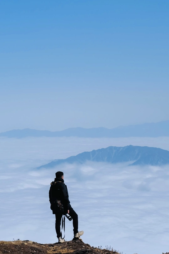 一个人坐在山顶上 眺望着云雾缭绕的山谷。