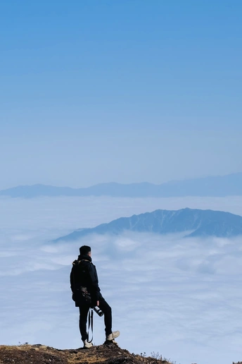 一个人坐在山顶上 眺望着云雾缭绕的山谷。