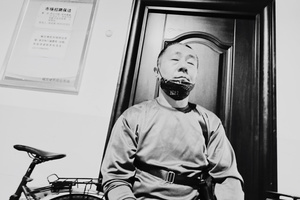 一张黑白照片 照片中一名男子戴着口罩坐在房间里的自行车前