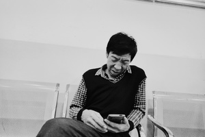 一张黑白照片 照片中一名男子坐在椅子上 手里拿着手机